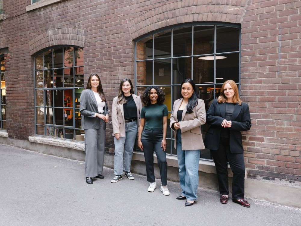 Five women from a Toronto PR and marketing agency standing outside a brick building in business-casual attire.